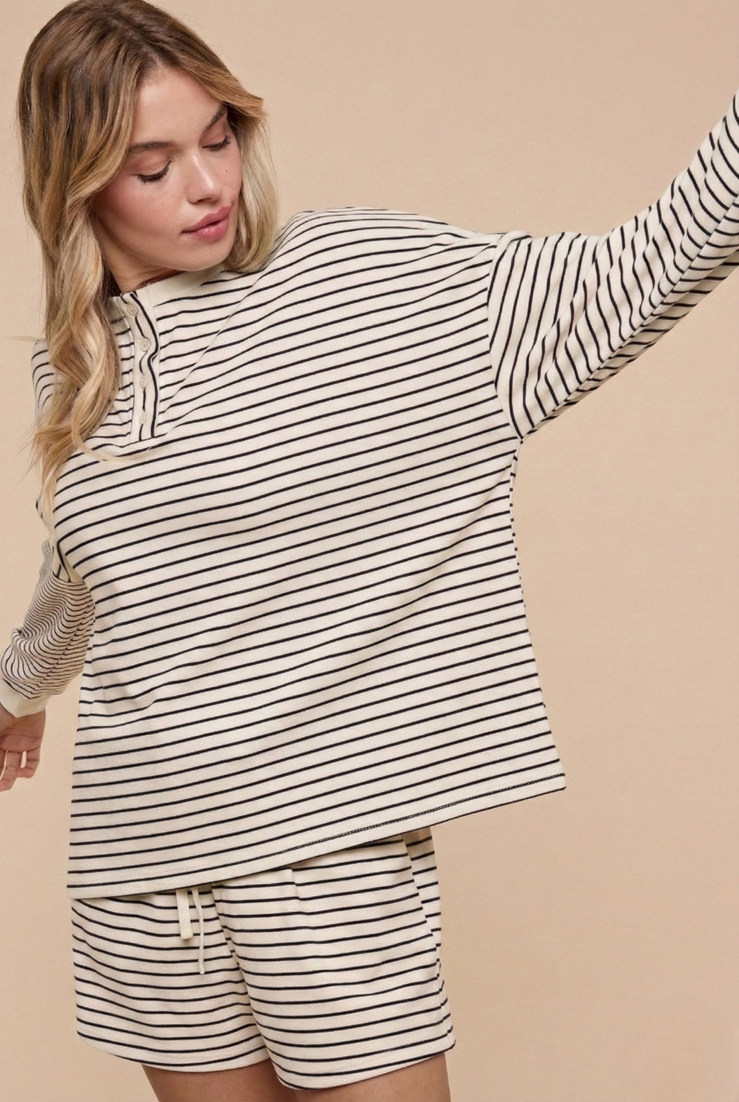 Woman wearing a striped long-sleeve top and shorts on a beige background