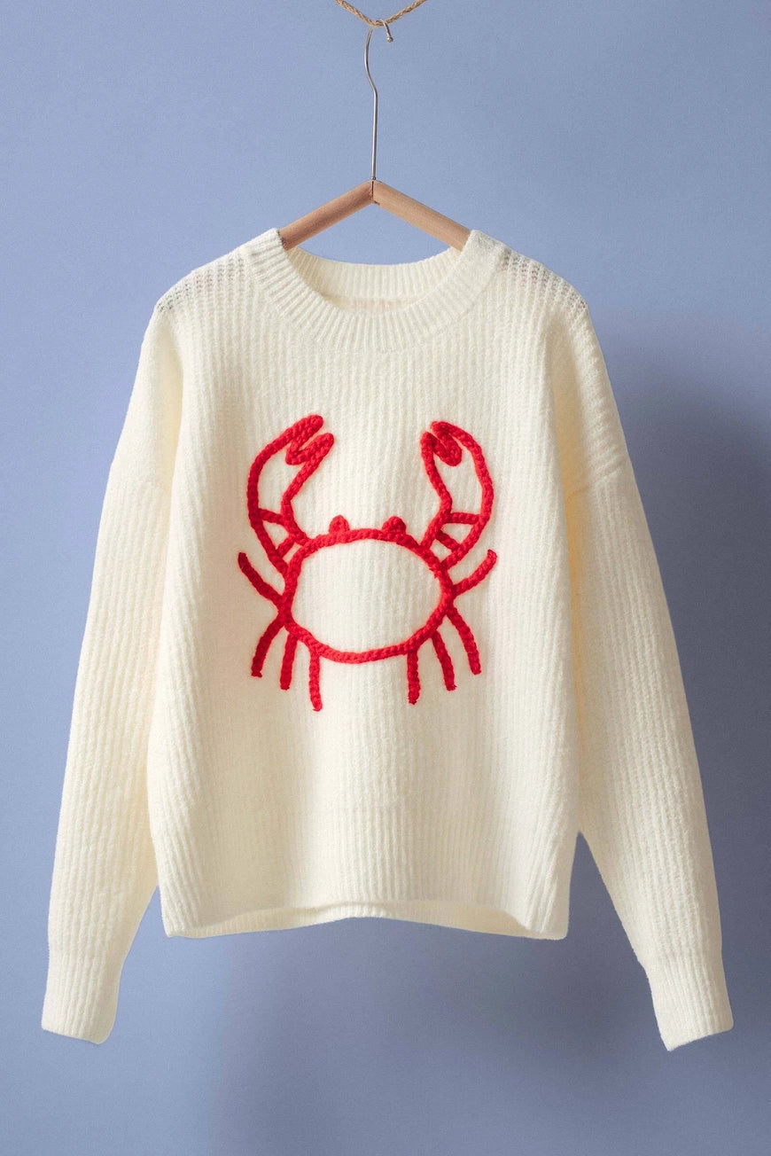 White sweater with a red crab design on a hanger against a purple background