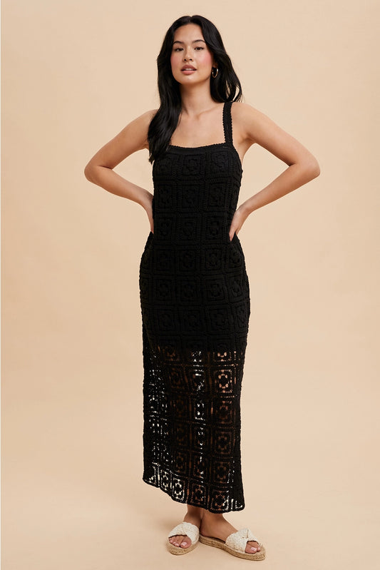 A woman standing in a studio setting, wearing a black square neck maxi dress with tank straps and a concealed side zipper.