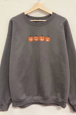 A dark gray crewneck sweatshirt hanging on a wooden hanger against a plain light background, featuring a row of four orange jack-o'-lantern faces across the chest.