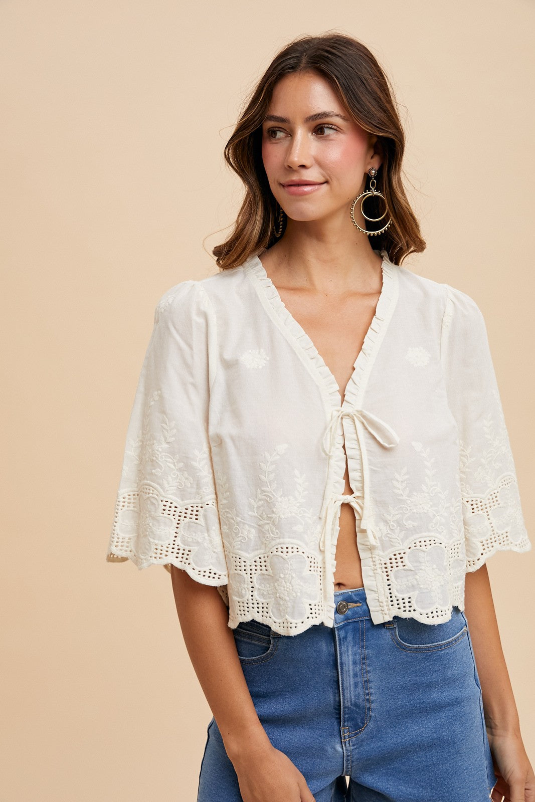 Woman wearing a white lace top and blue jeans against a beige background