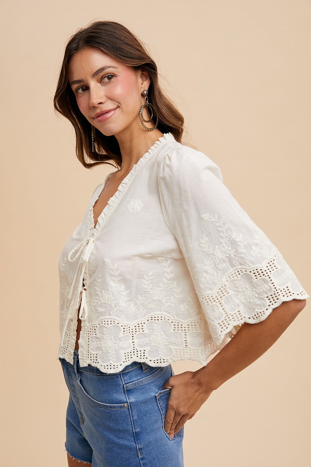 Woman wearing a white lace top and blue jeans on a beige background