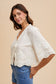 Woman wearing a white lace top and blue jeans on a beige background