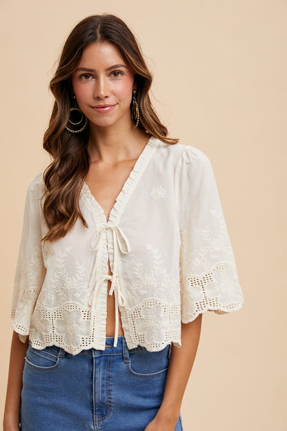 Woman wearing a white lace top and blue jeans on a beige background