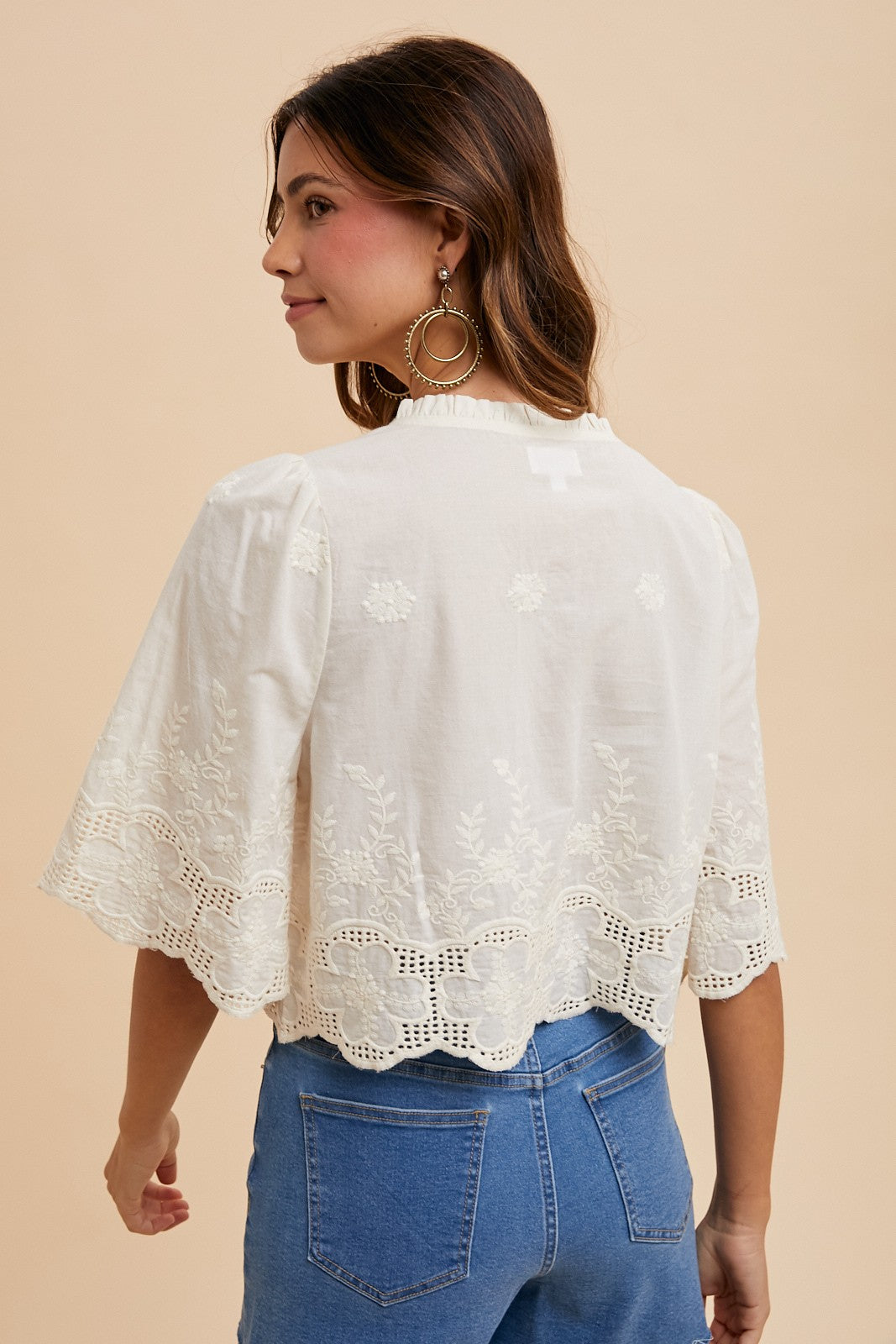 Woman wearing a white lace top and blue jeans on a beige background