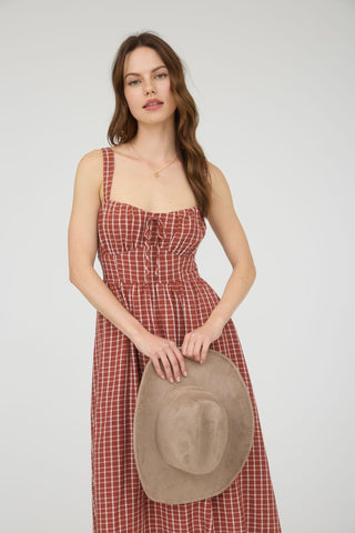 Woman in a red checkered dress holding a beige hat against a white background