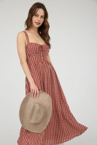 Woman wearing a red checkered dress holding a beige hat against a white background