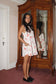 Woman in a floral dress standing in front of a wooden wardrobe.