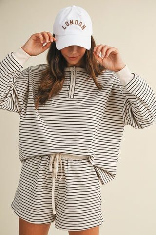 Person wearing a striped outfit and 'London' cap on a beige background