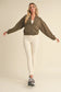 Woman wearing a green bomber jacket and white leggings on a beige background
