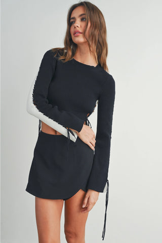 A female model wearing a long sleeve white and black crop top with tie-up sleeves and a crew neckline.