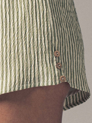Close-up of a green and white striped shirt with brown buttons on a neutral background