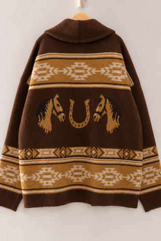 A brown knit poncho sweater with a high collar, featuring a central design of two horse heads facing each other around a horseshoe, bordered by geometric patterns in tan and cream.