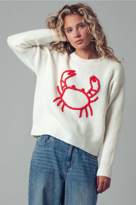 Woman wearing a white sweater with a red crab design on a gray background