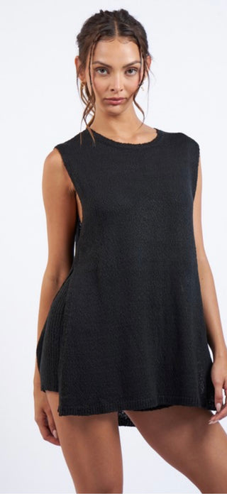 A female model wearing a black knit sleeveless tunic top with an open neckline and paired with elastic waste band shorts.