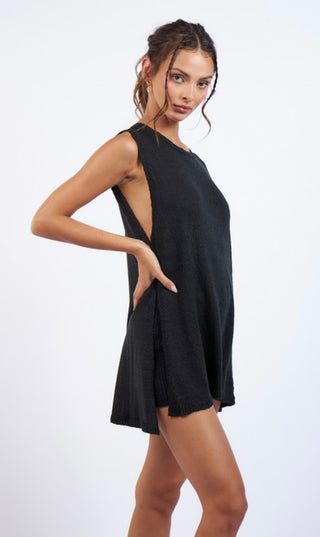 A female model wearing a black knit sleeveless tunic top with an open neckline and paired with elastic waste band shorts.