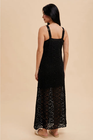 A woman standing in a studio setting, wearing a black square neck maxi dress with tank straps and a concealed side zipper.