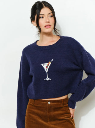 A woman wearing a navy blue cropped knit sweater with a white embroidered martini glass graphic on the chest, paired with brown corduroy pants, against a plain white background.