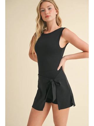 Woman wearing a black romper with a bow detail on a beige background