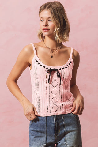 A woman wearing a pink ribbon-knit tank top with black tie and spaghetti straps, featuring a V-neckline and short sleeves.