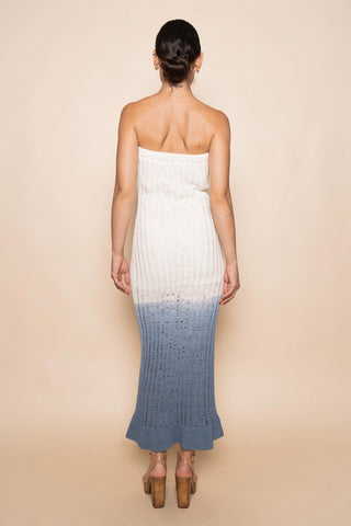 Woman wearing a strapless dress with a white top and blue gradient skirt on a beige background